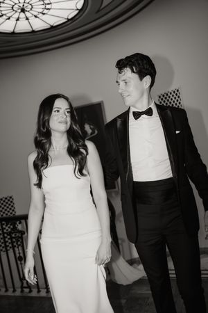 A black and white wedding photo of a couple walking together, with the bride in white gown and groom in black tuxedo.