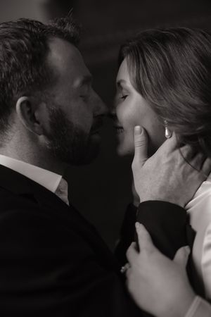 Intimate black and white portrait of a romantic couple about to kiss, with gentle hand caressing face.