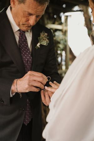 A close-up of hands exchanging rings during an outdoor wedding ceremony.