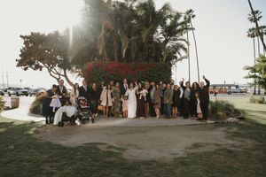 Wedding party poses for a group photo under a tree at a tropical beach location during sunset.