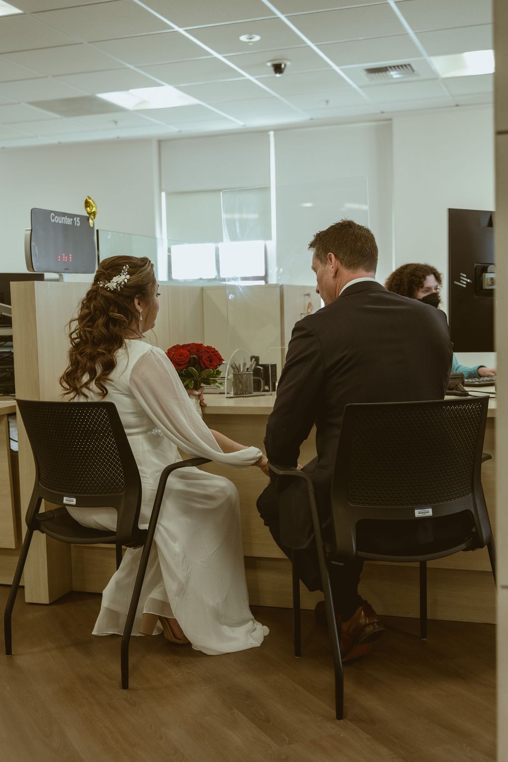 Two people sit at a desk in an office during a civil ceremony with red roses.