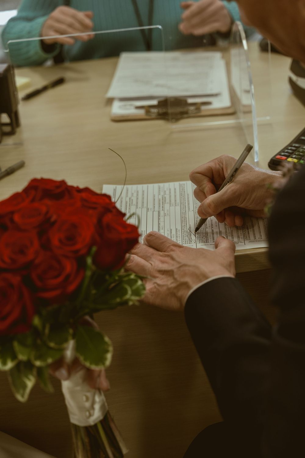 Hands signing paperwork with a bouquet of red roses on the desk.