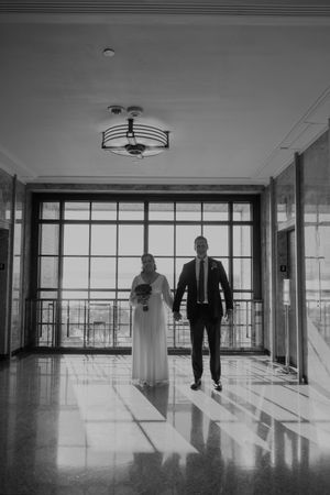A couple stands in silhouette against large windows in an elegant hallway.