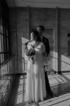 A romantic black and white portrait of a couple standing in dramatic window light.