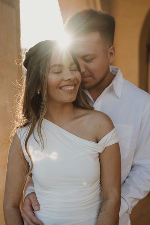 Intimate sunlit portrait of a couple in white clothing sharing a tender moment.