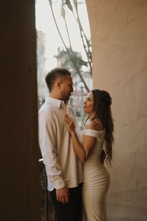 Romantic couple in formal attire sharing an intimate moment against a neutral wall.