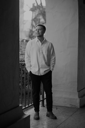 Black and white portrait of person in white shirt standing in covered walkway.