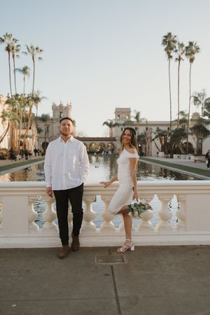 Couple walking along decorative balustrade with palm trees in background at sunset.