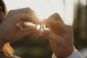 Close-up of hands holding wedding rings in golden sunlight.