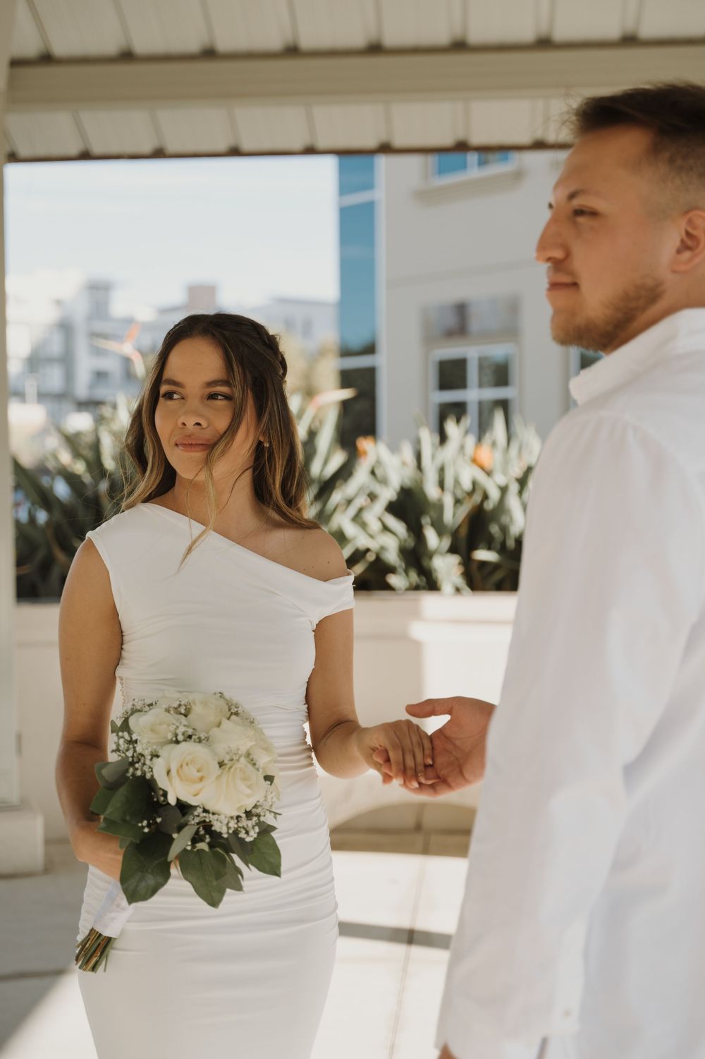 A casual outdoor photoshoot with a couple in white holding a bouquet.