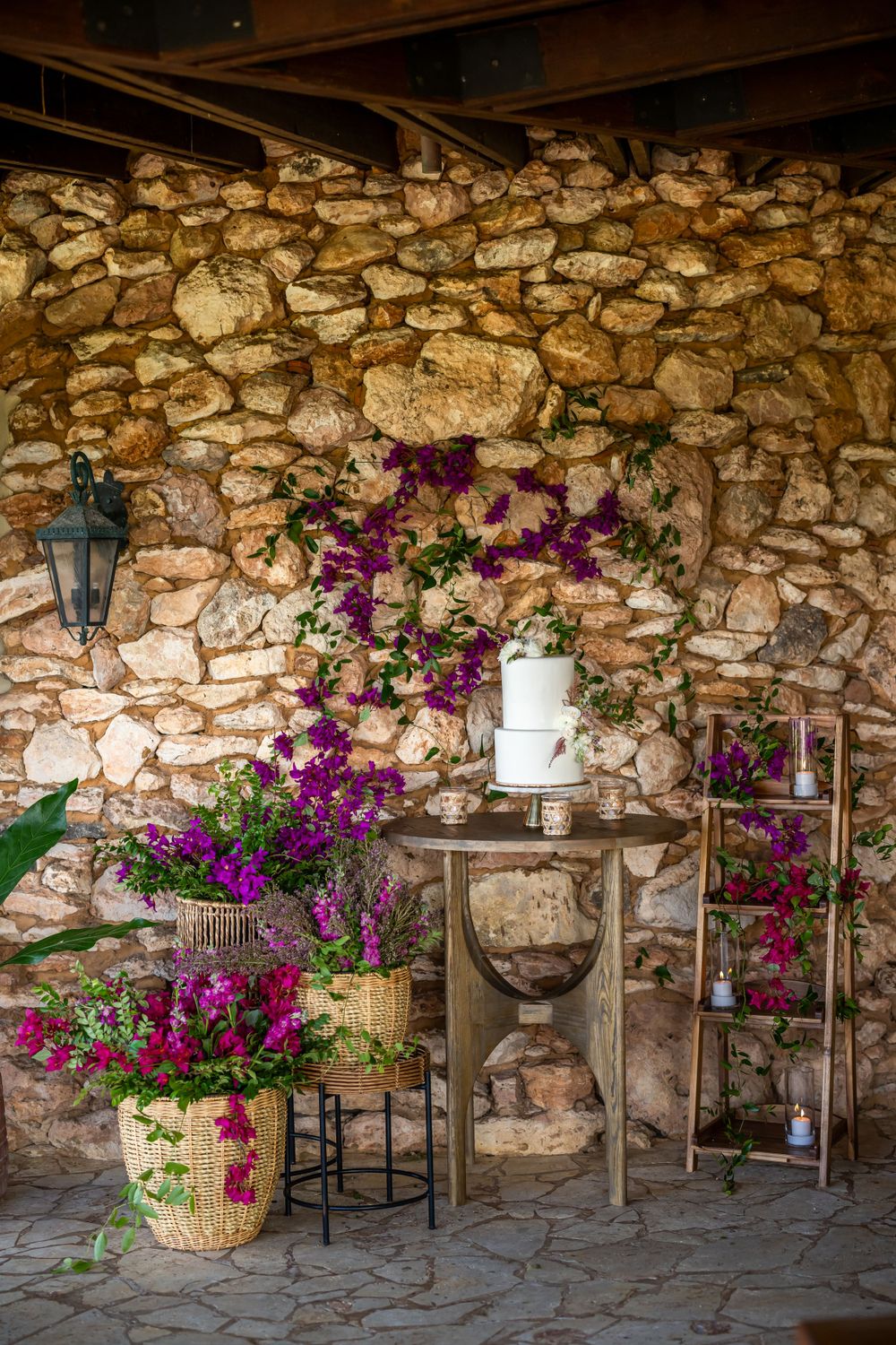 Stone wall decorated with vibrant purple bougainvillea flowers and rustic wedding decor.