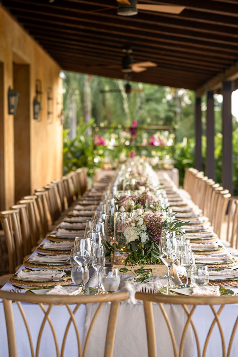 Formal dining table set for wedding reception with white linens and floral arrangements under covered porch.