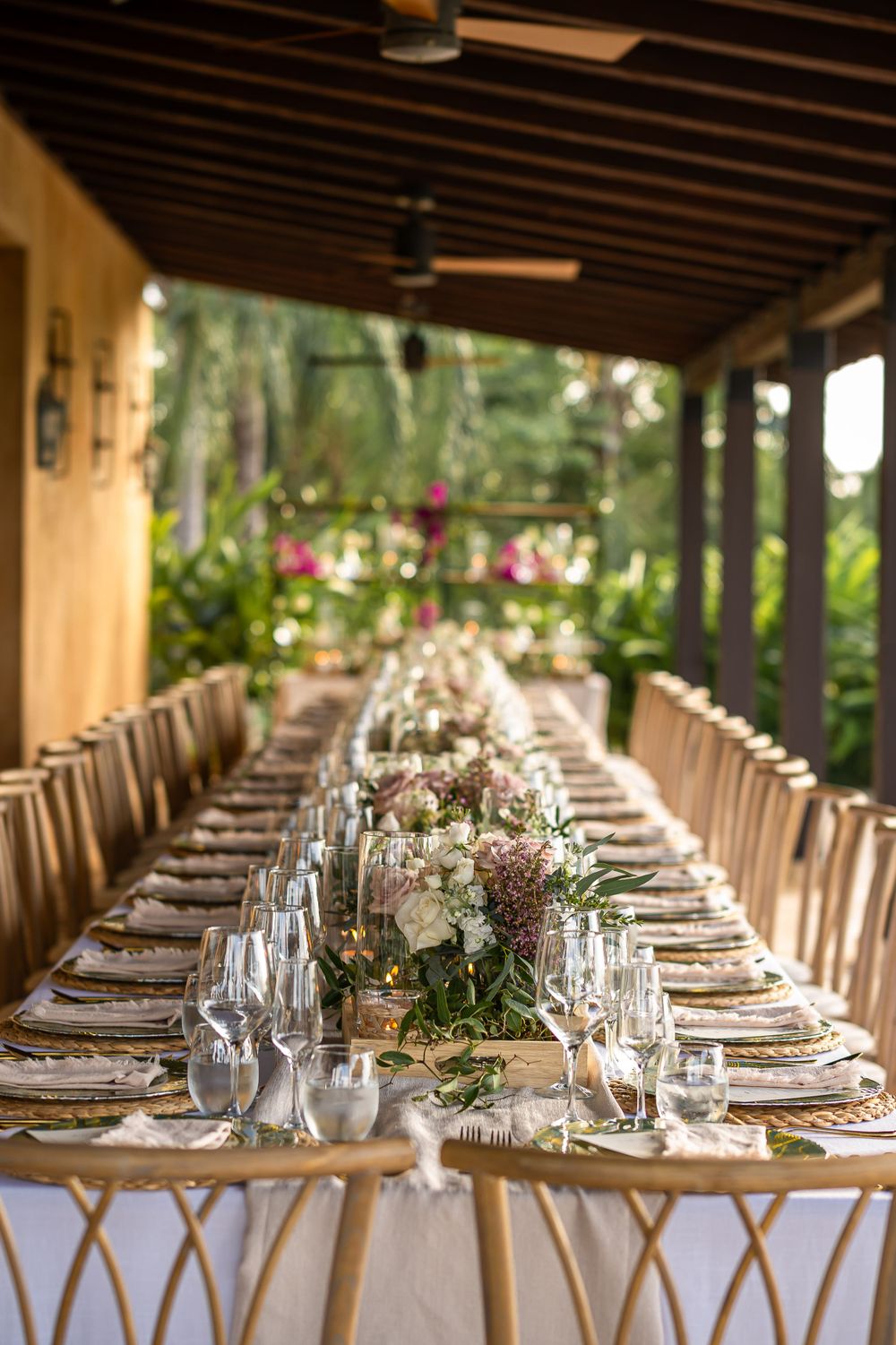 Elegant outdoor wedding reception table with white linens and gold chairs under wooden beamed ceiling.
