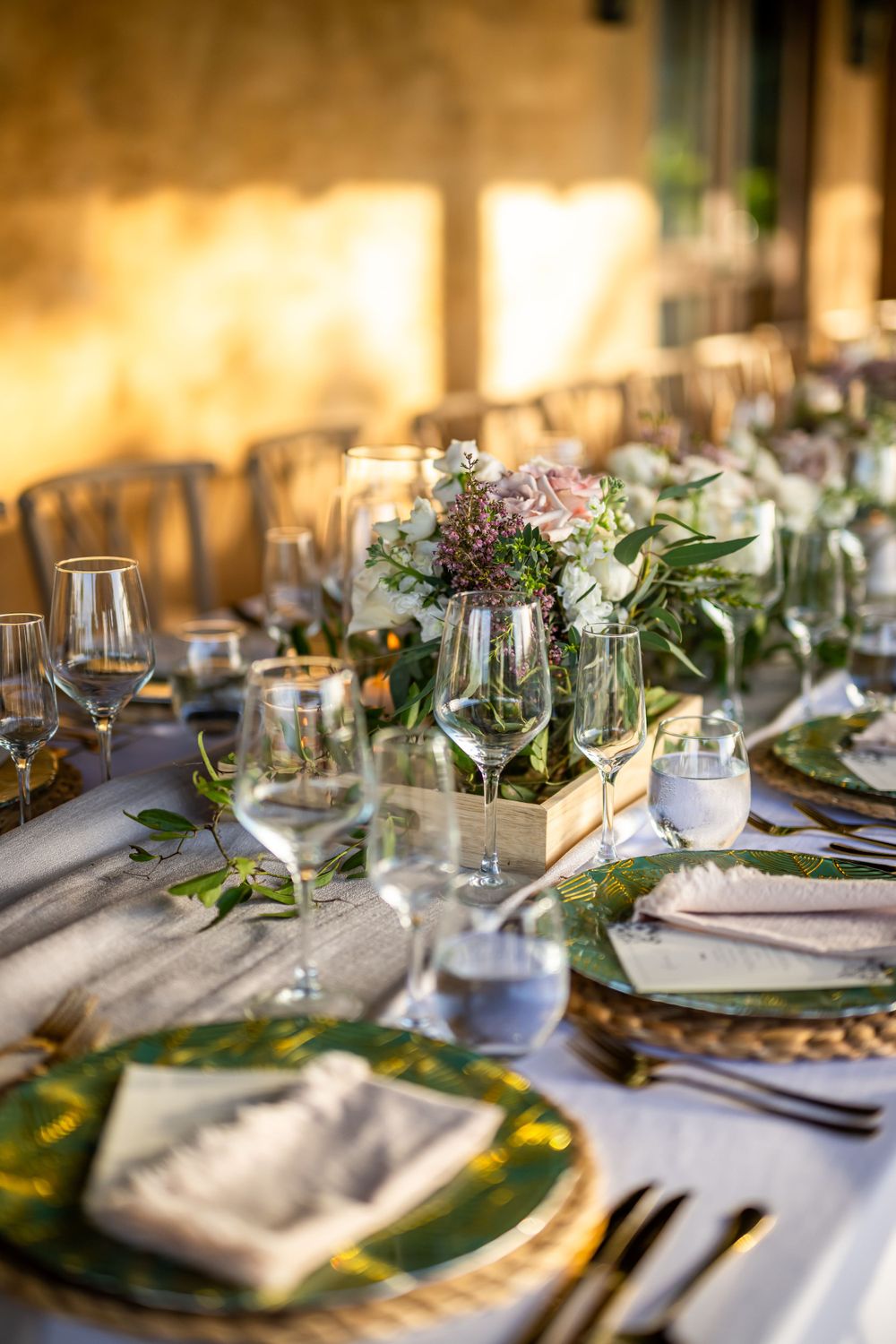 Sunlit wedding table setting with woven chargers, green plates and delicate floral centerpieces.