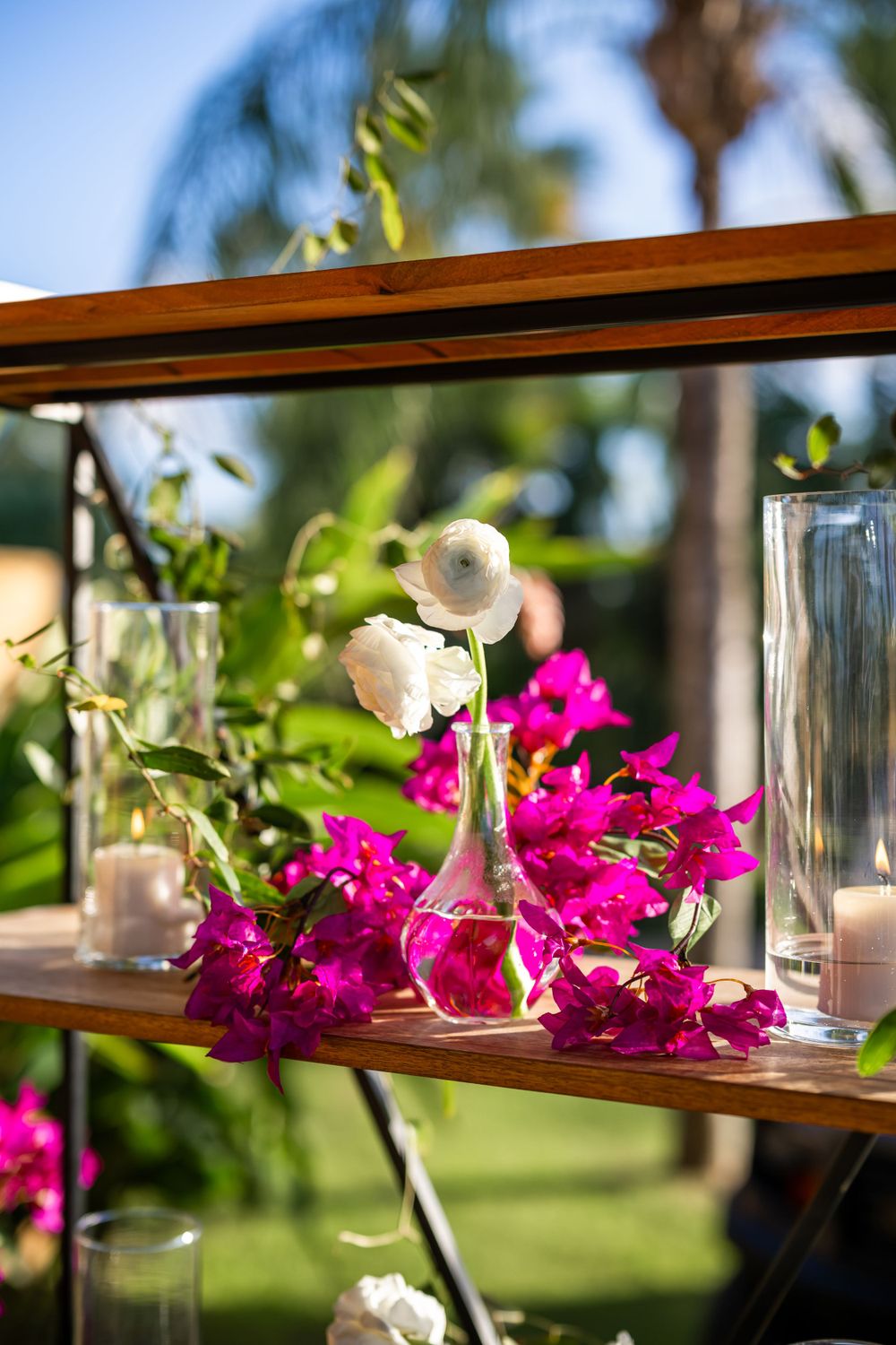 Pink bougainvillea flowers and white roses arranged on wooden shelves with glass vases.