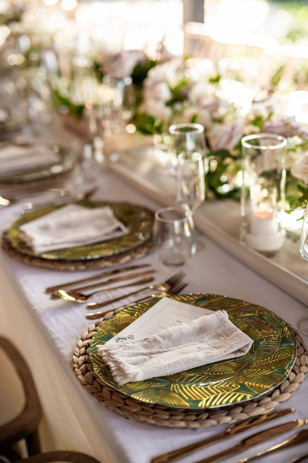 Formal place setting with decorative green charger plates and white napkins on wedding table.