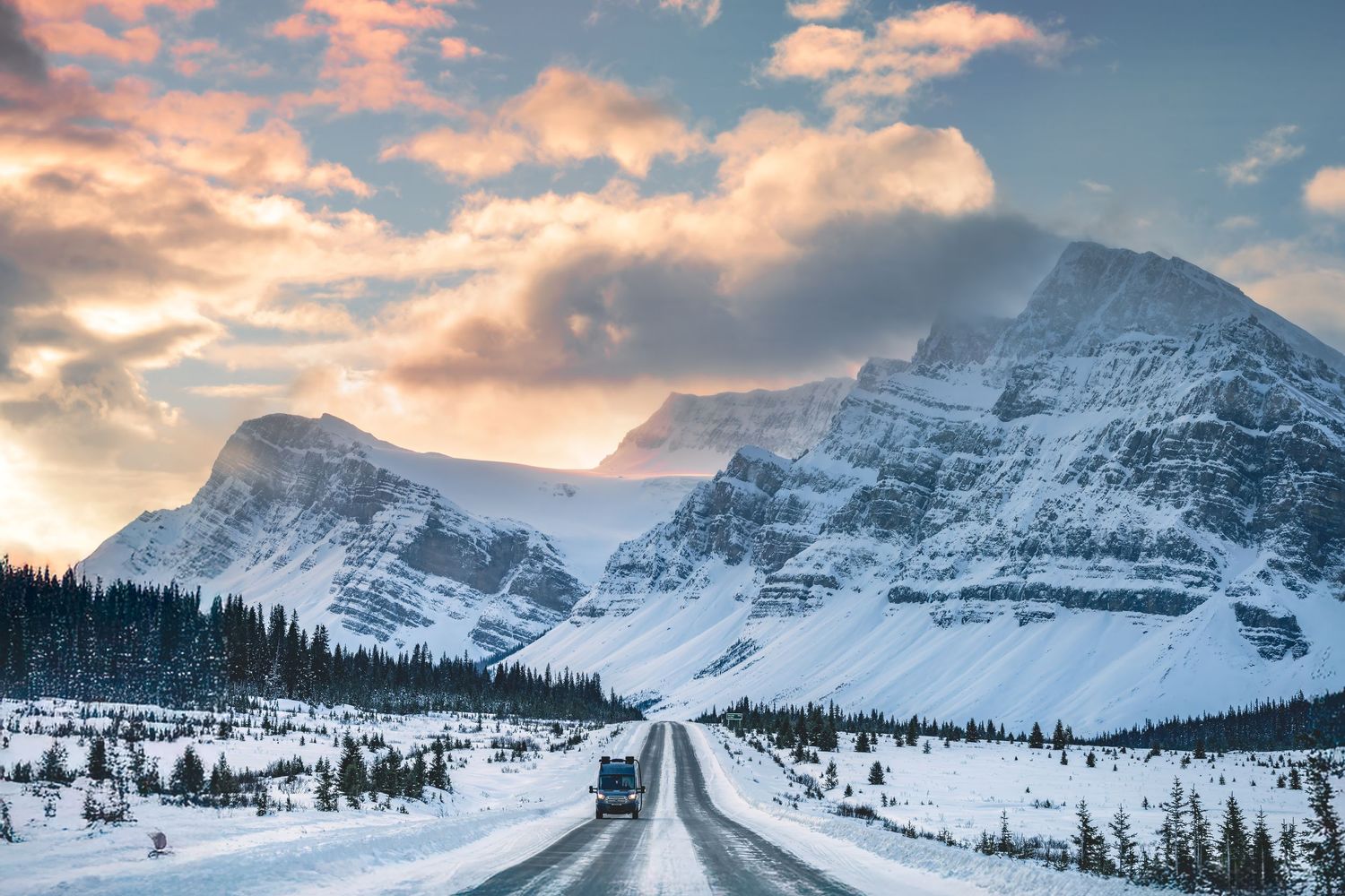 Snowy mountain highway winding through a winter wilderness landscape under dramatic cloudy skies.