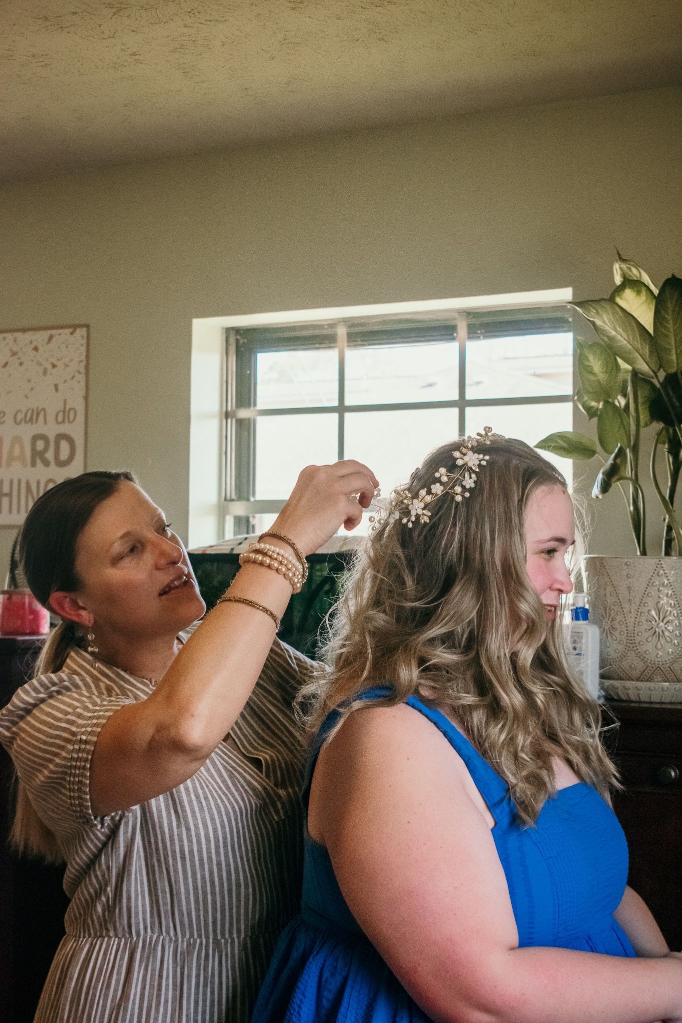 A hair stylist arranges delicate hairpieces on someone wearing a blue dress during wedding preparations.