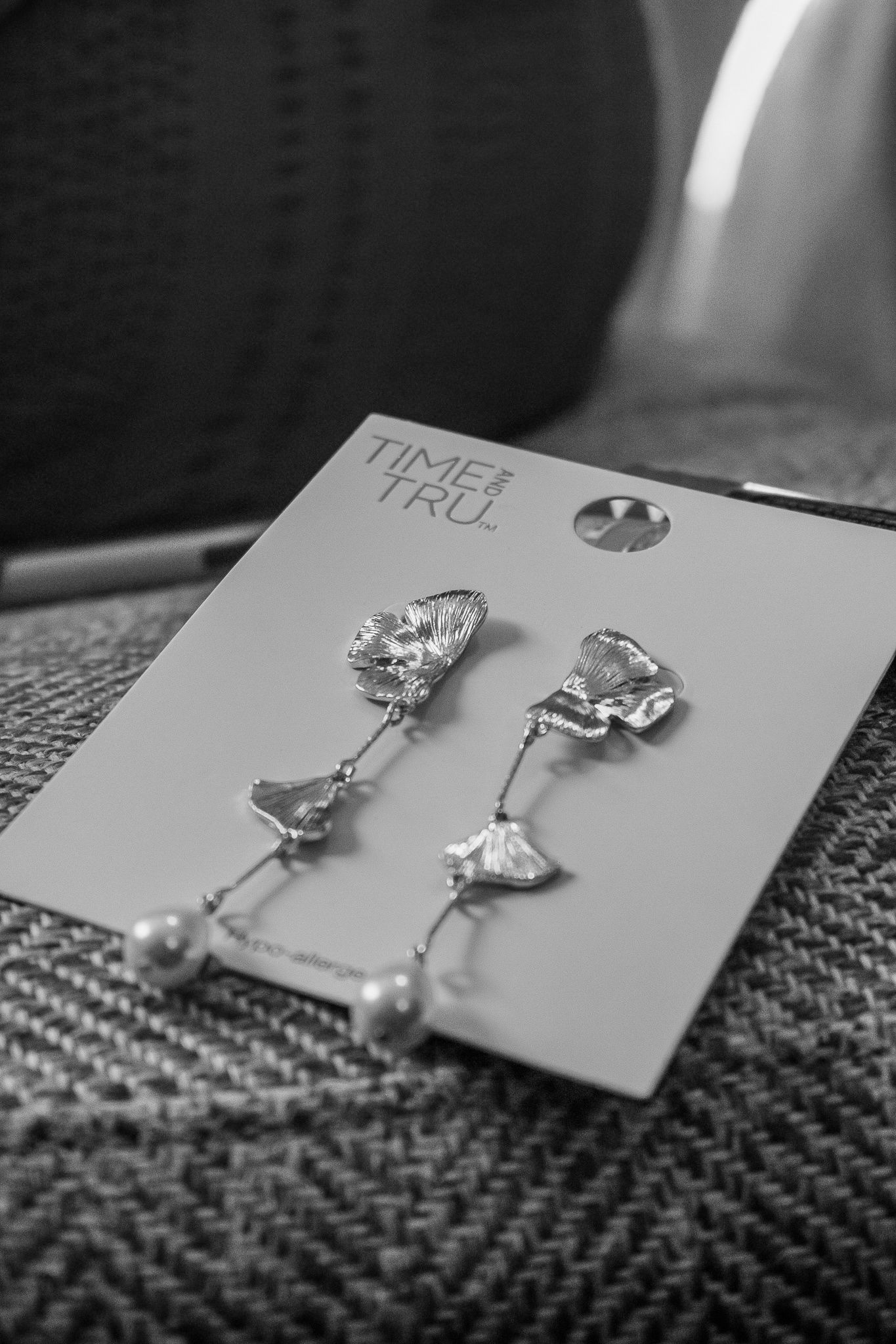 Black and white detail shot of delicate silver drop earrings on a textured surface.