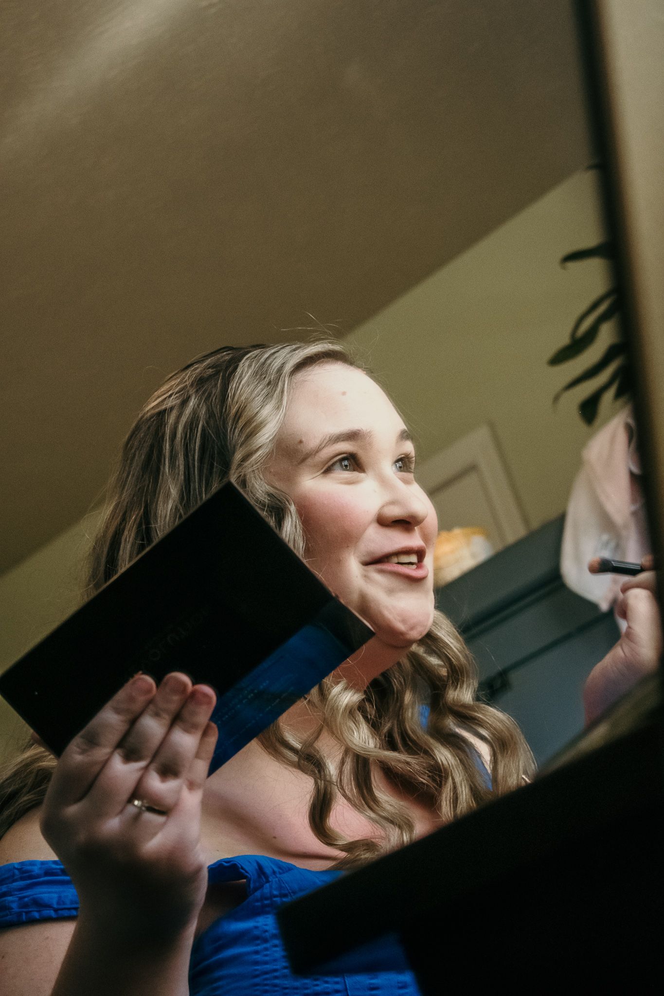 Woman in blue dress reacts with joy while holding a letter or card.