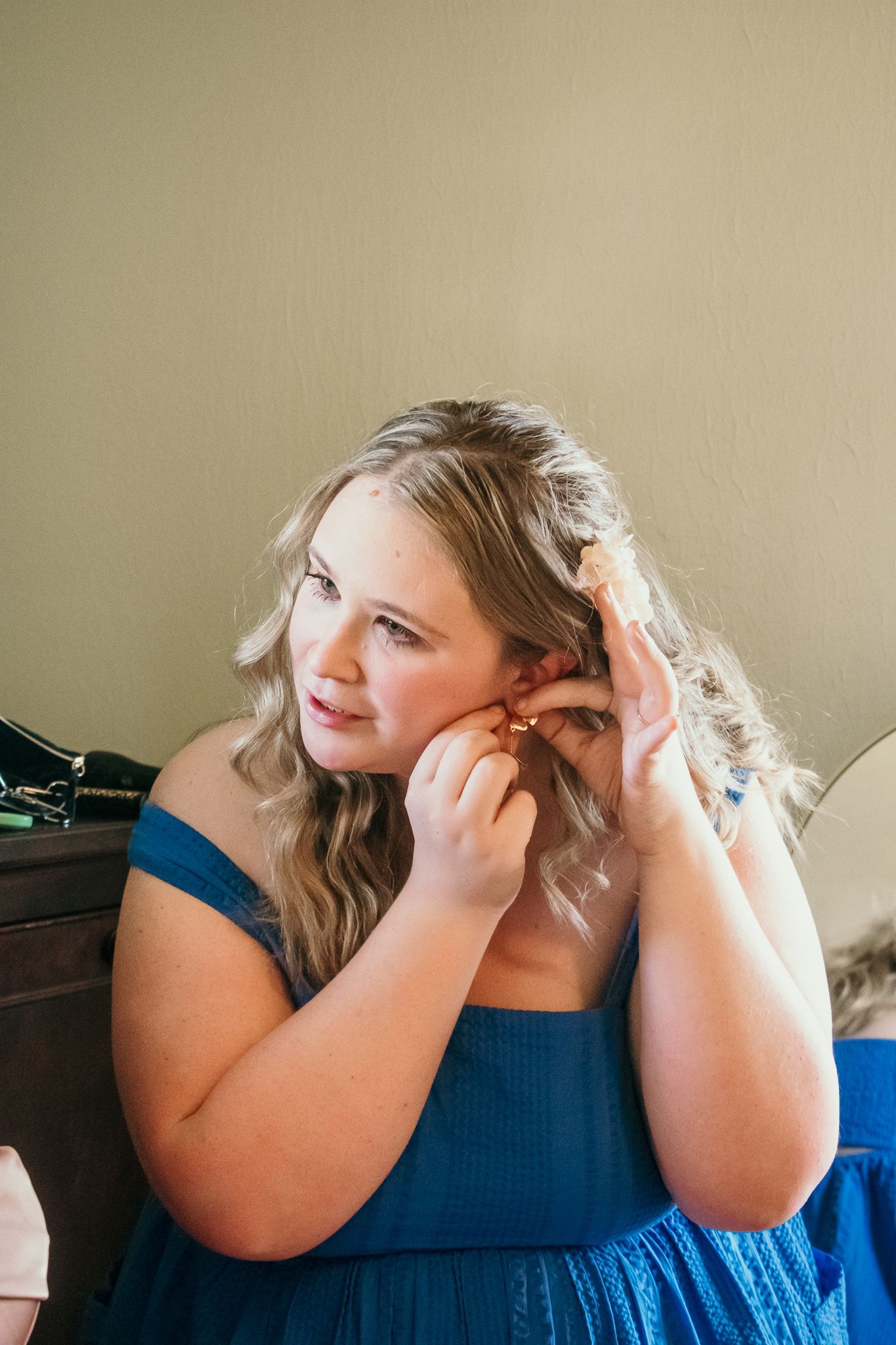 A person in a navy blue dress puts on earrings while getting ready.
