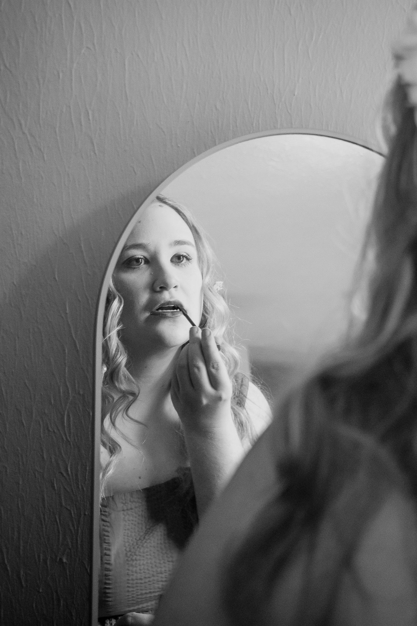 Artistic black and white reflection of someone applying makeup in an arched mirror.