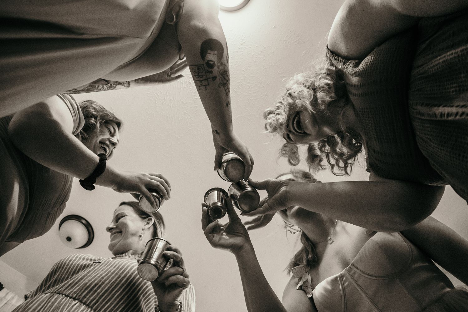A monochromatic low-angle view of a group holding drinks together in a circle for a celebratory toast.