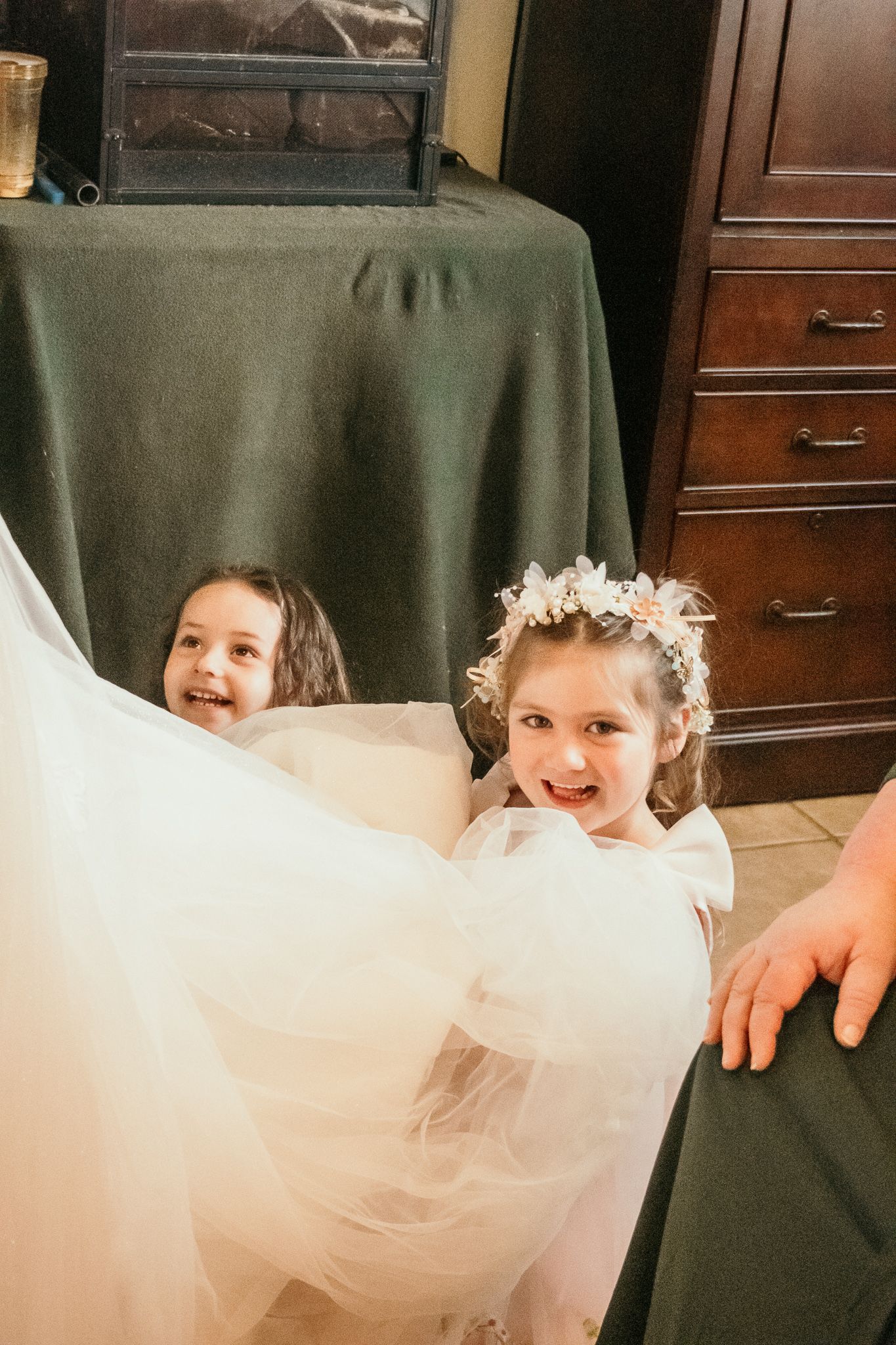 Young children giggling and peeking through flowing white tulle fabric at a formal event.
