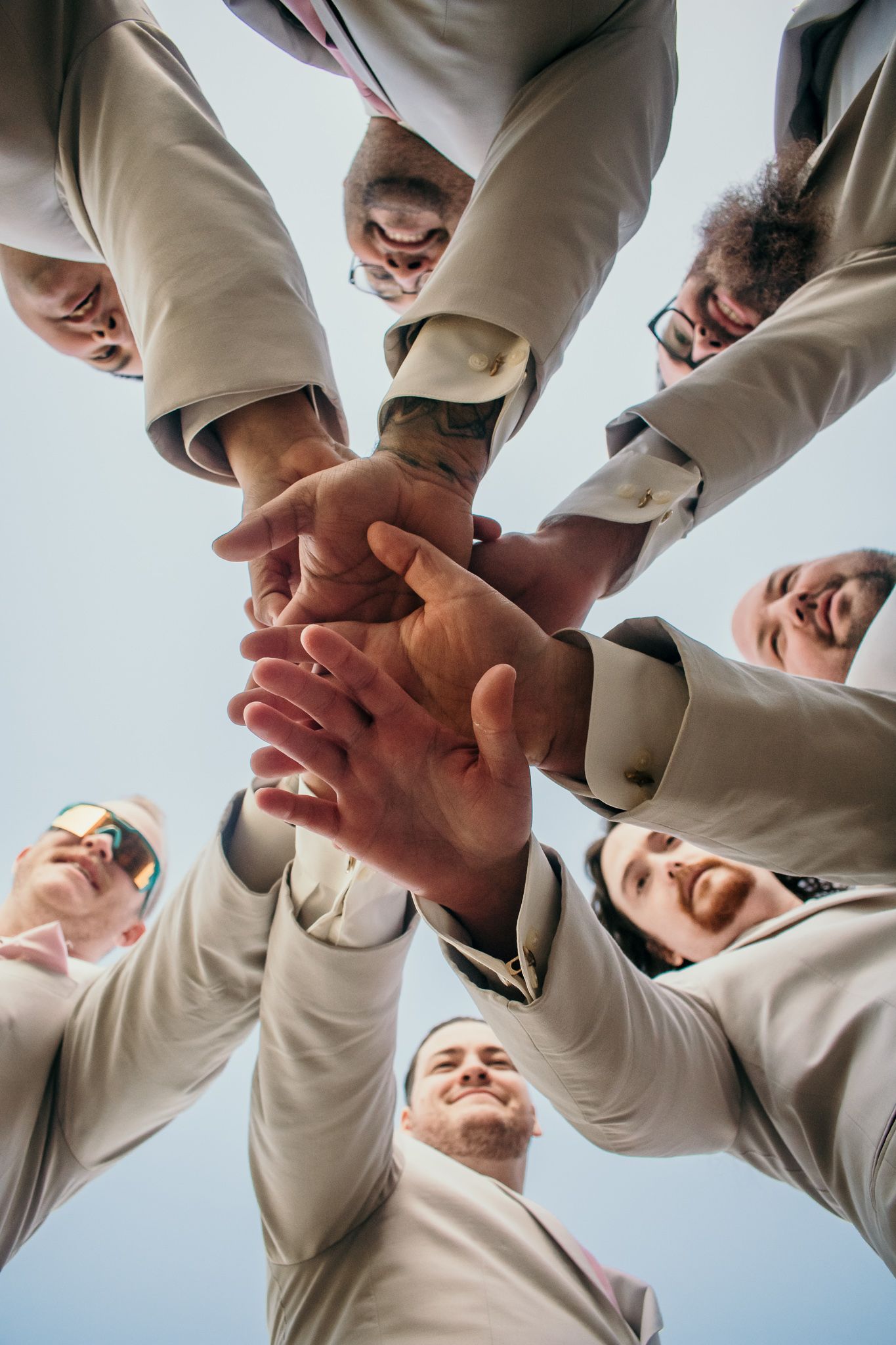 A team huddle with hands joined together in unity against a bright sky background.
