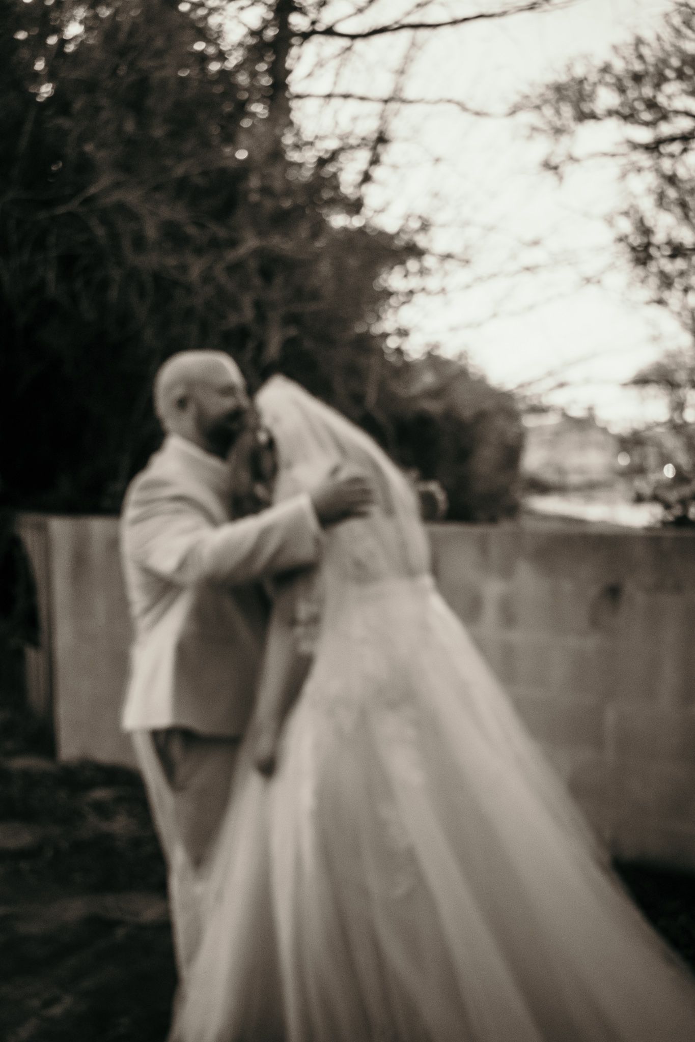 A romantic black and white wedding moment captured outdoors with flowing white dress and veil.