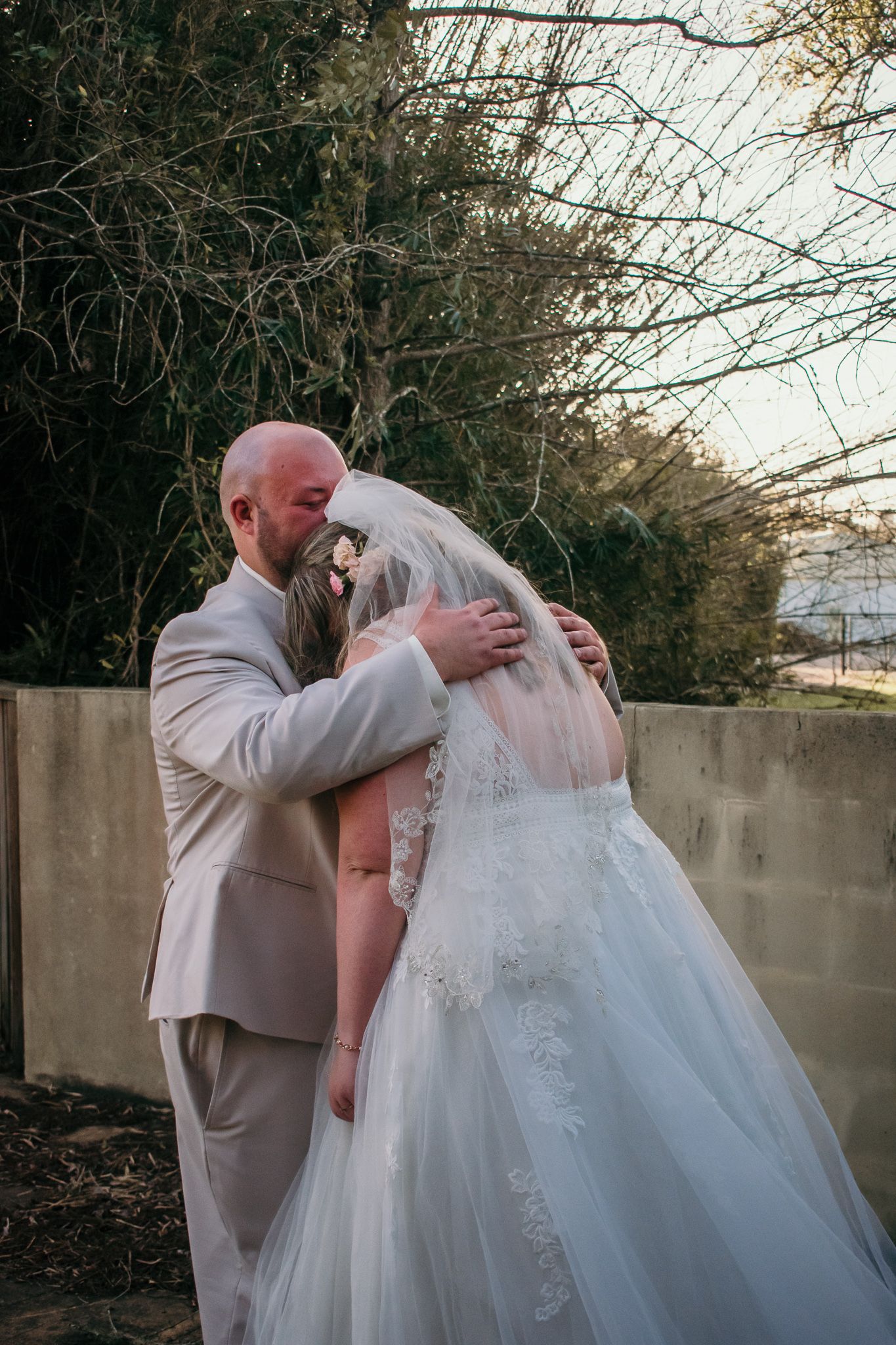 Tender embrace between couple in wedding attire during outdoor portrait session.