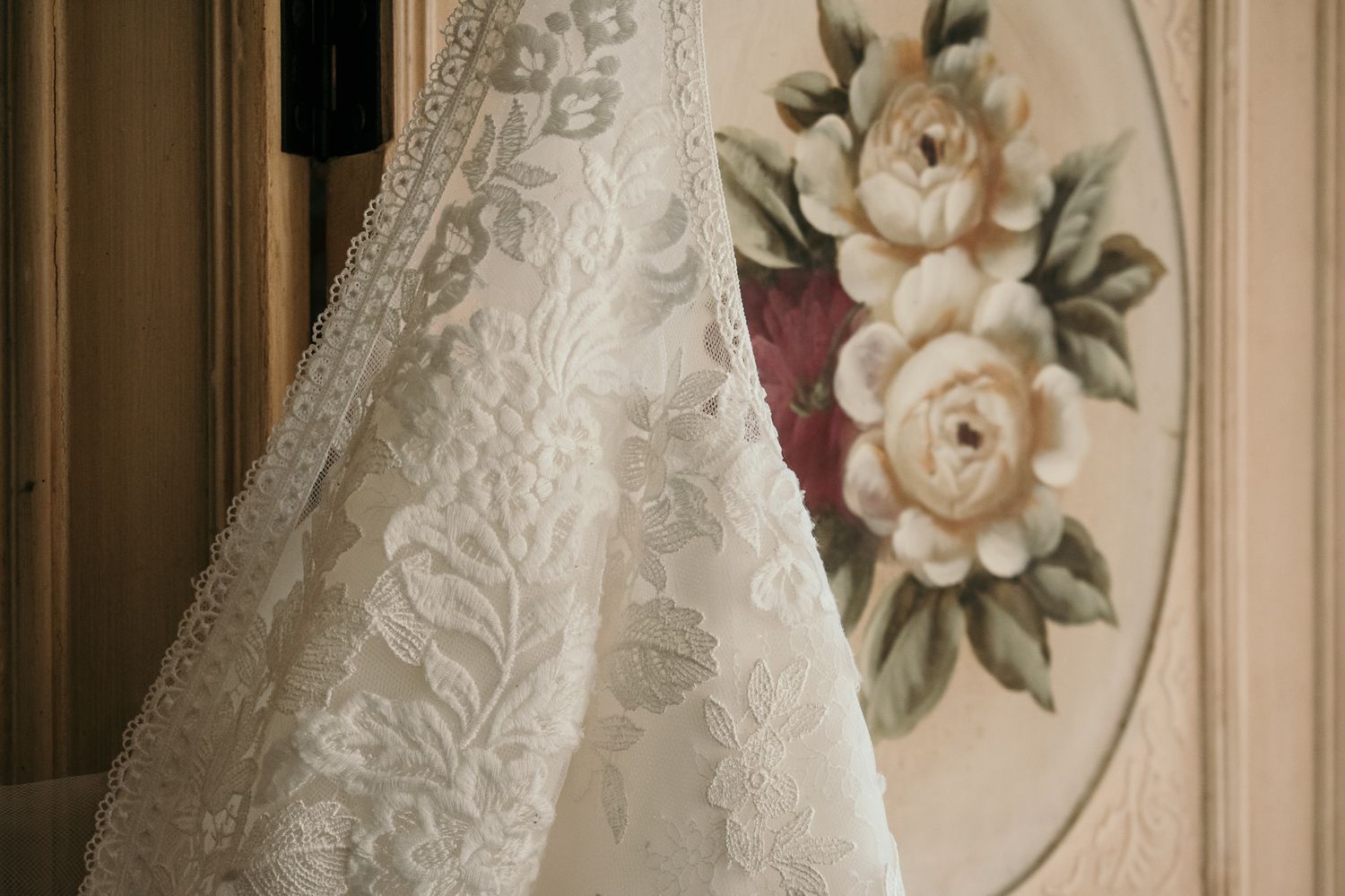 Delicate white lace detail of a wedding dress against a floral wallpaper background.
