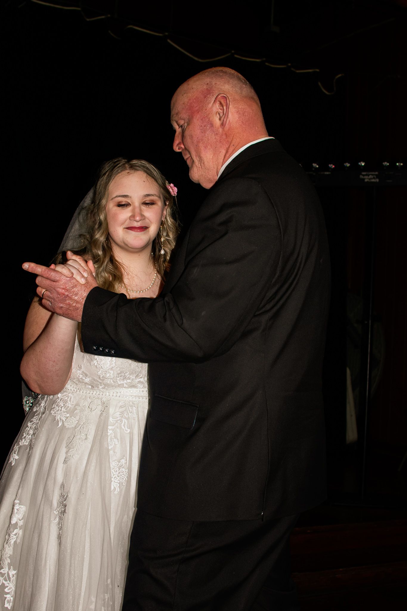 A tender father-daughter dance moment at a wedding reception in dim lighting.