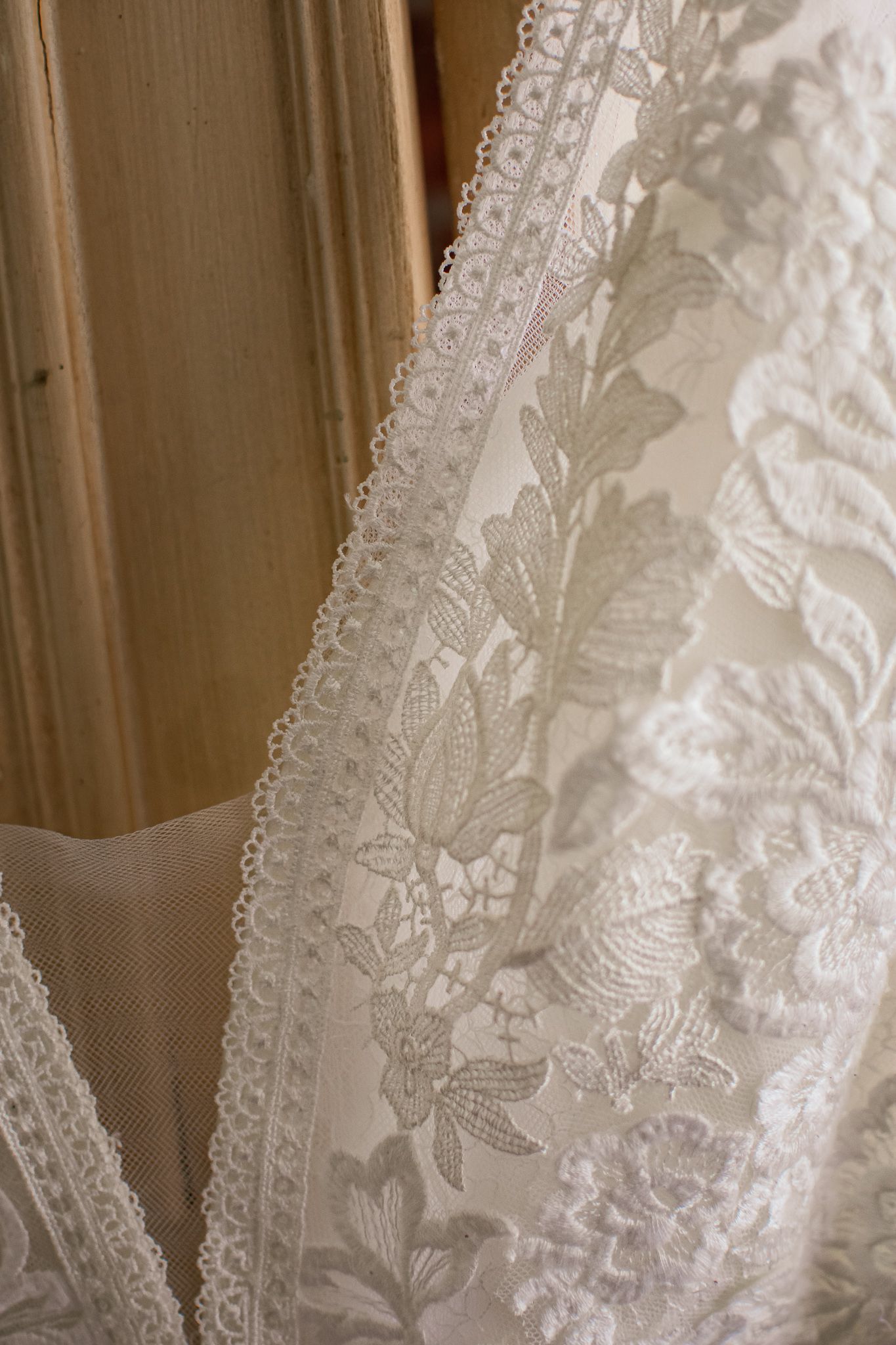 Close-up detail of delicate white lace and floral embroidery on a wedding dress fabric.