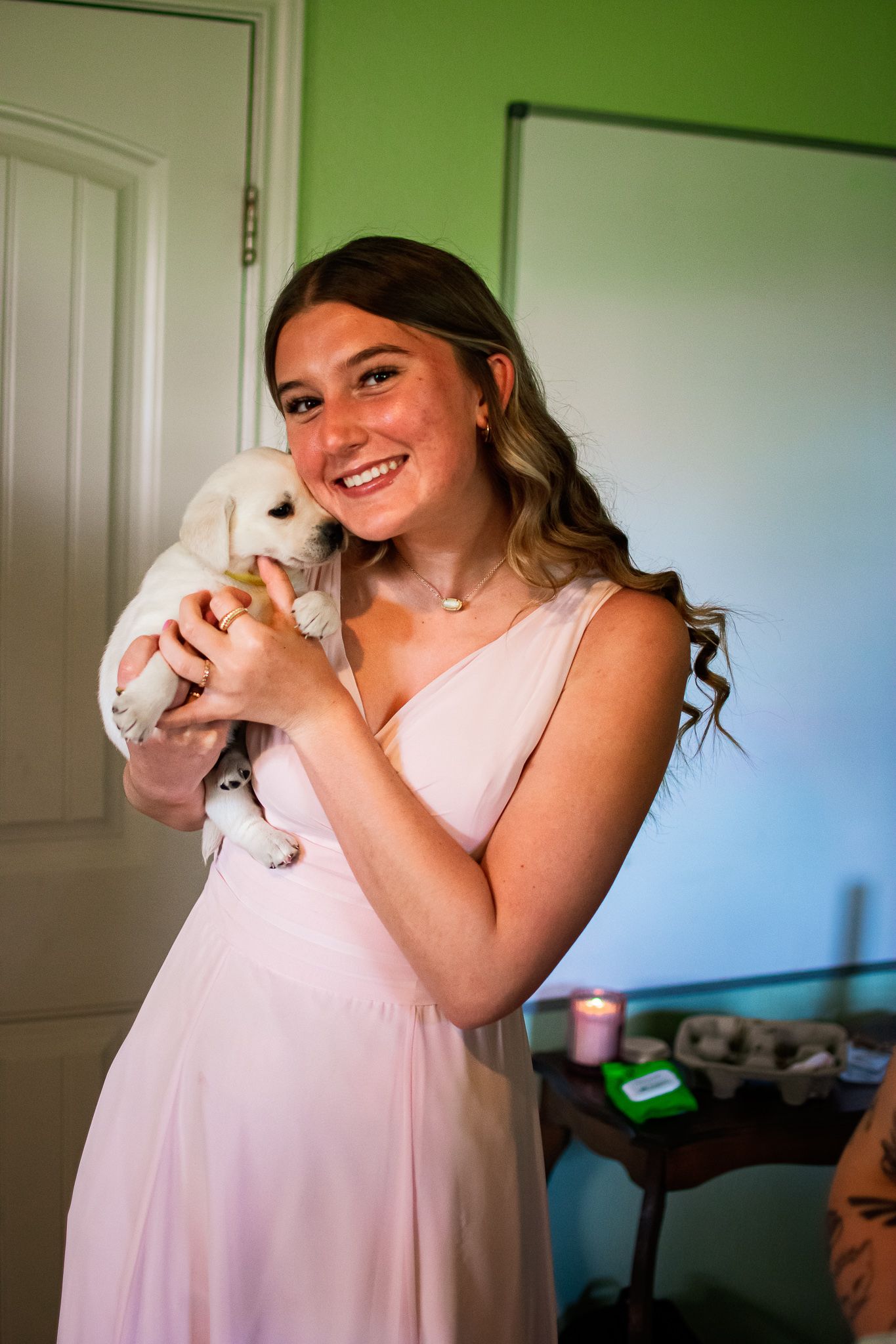 A person in a pink dress holds a white bunny while standing in front of a green wall.
