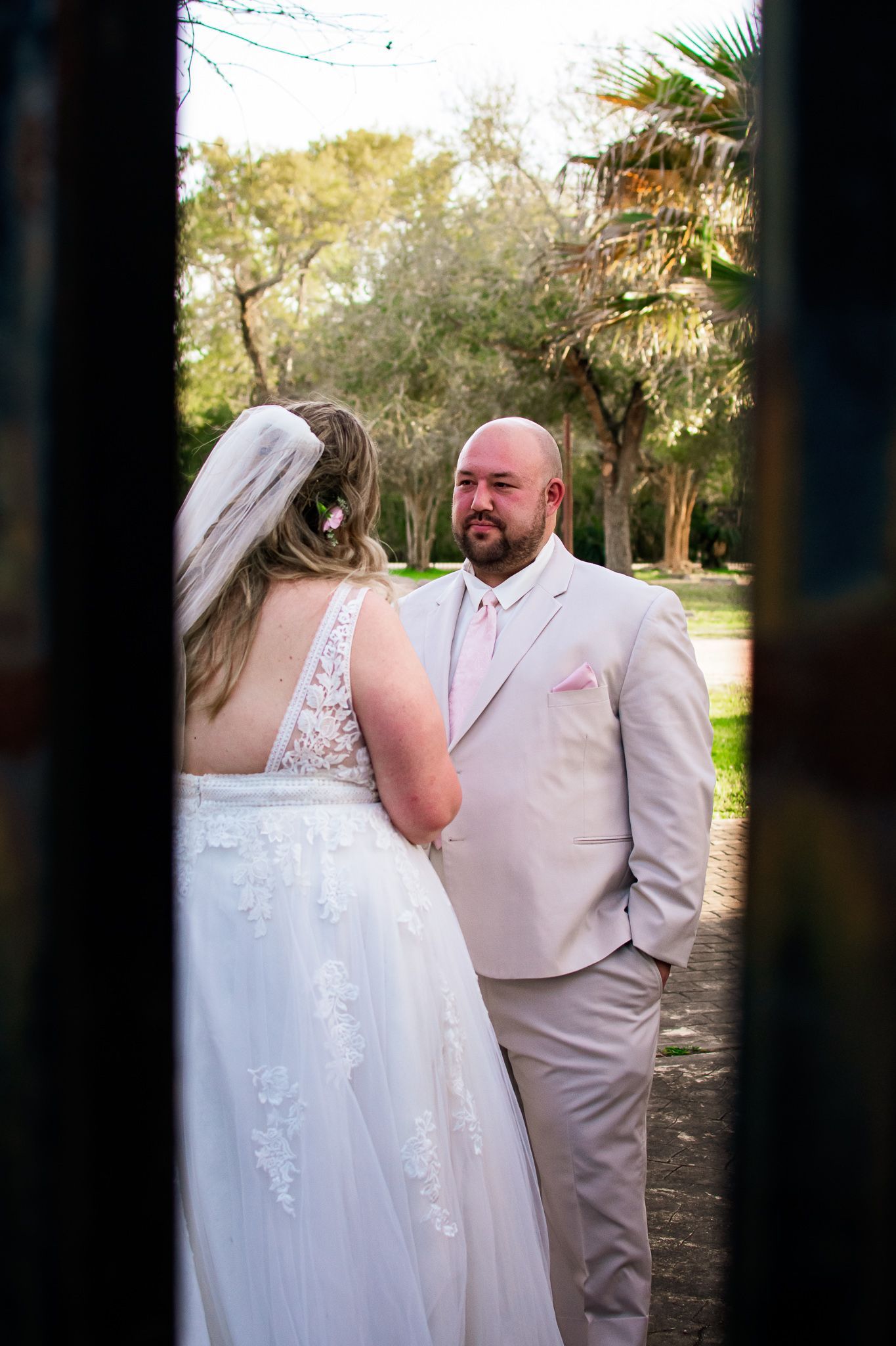 A couple shares a moment during their outdoor wedding ceremony wearing a white dress and light beige suit.