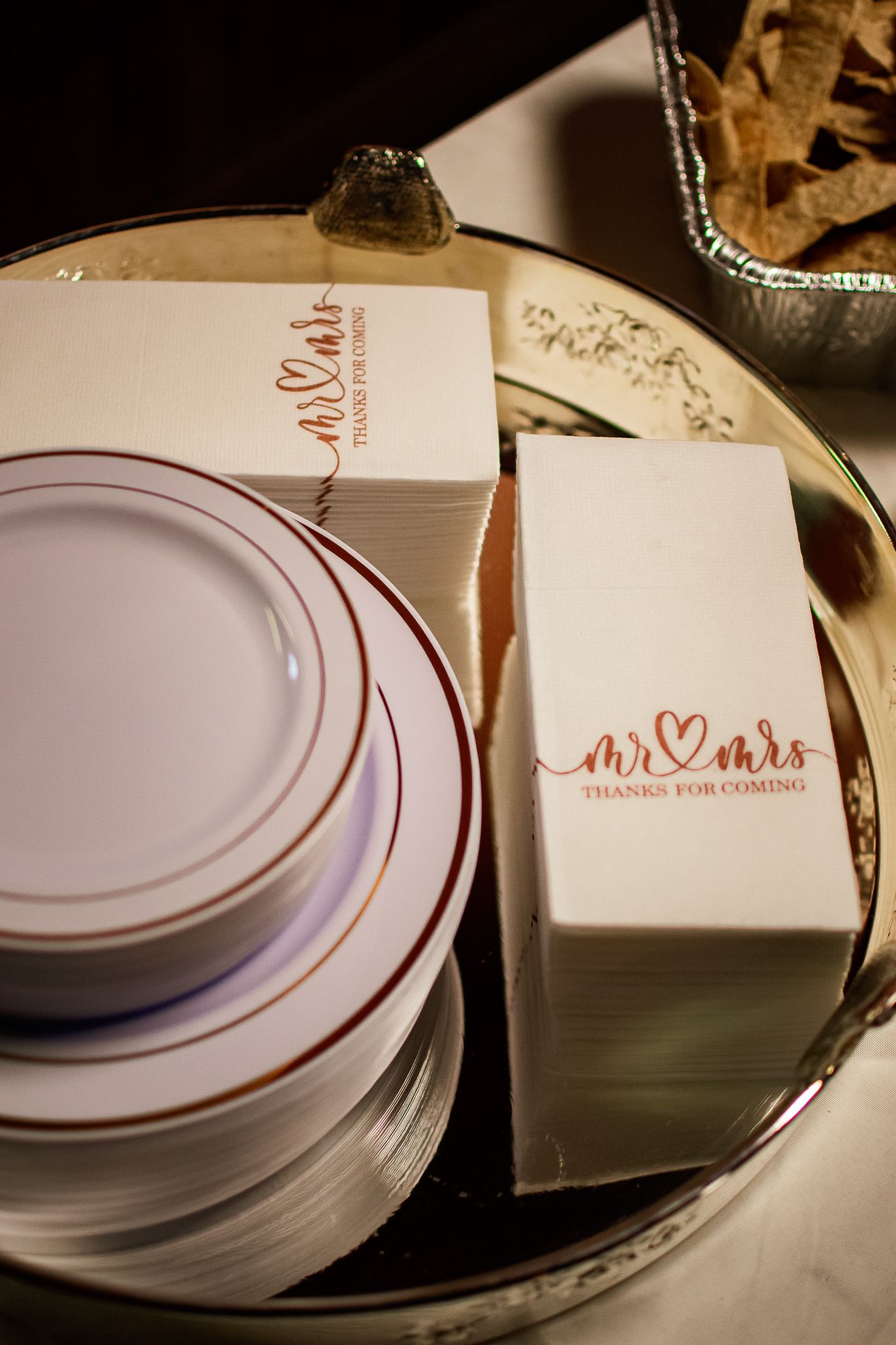 White disposable plates and wedding favor boxes with 'Mr & Mrs' text in rose gold lettering arranged on a table.