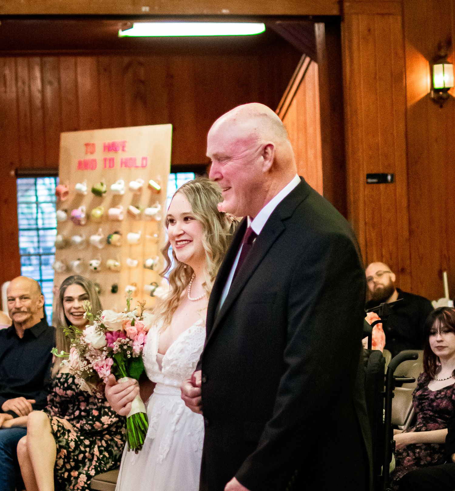 A wedding ceremony moment in a wood-paneled room with warm lighting and gathered guests.