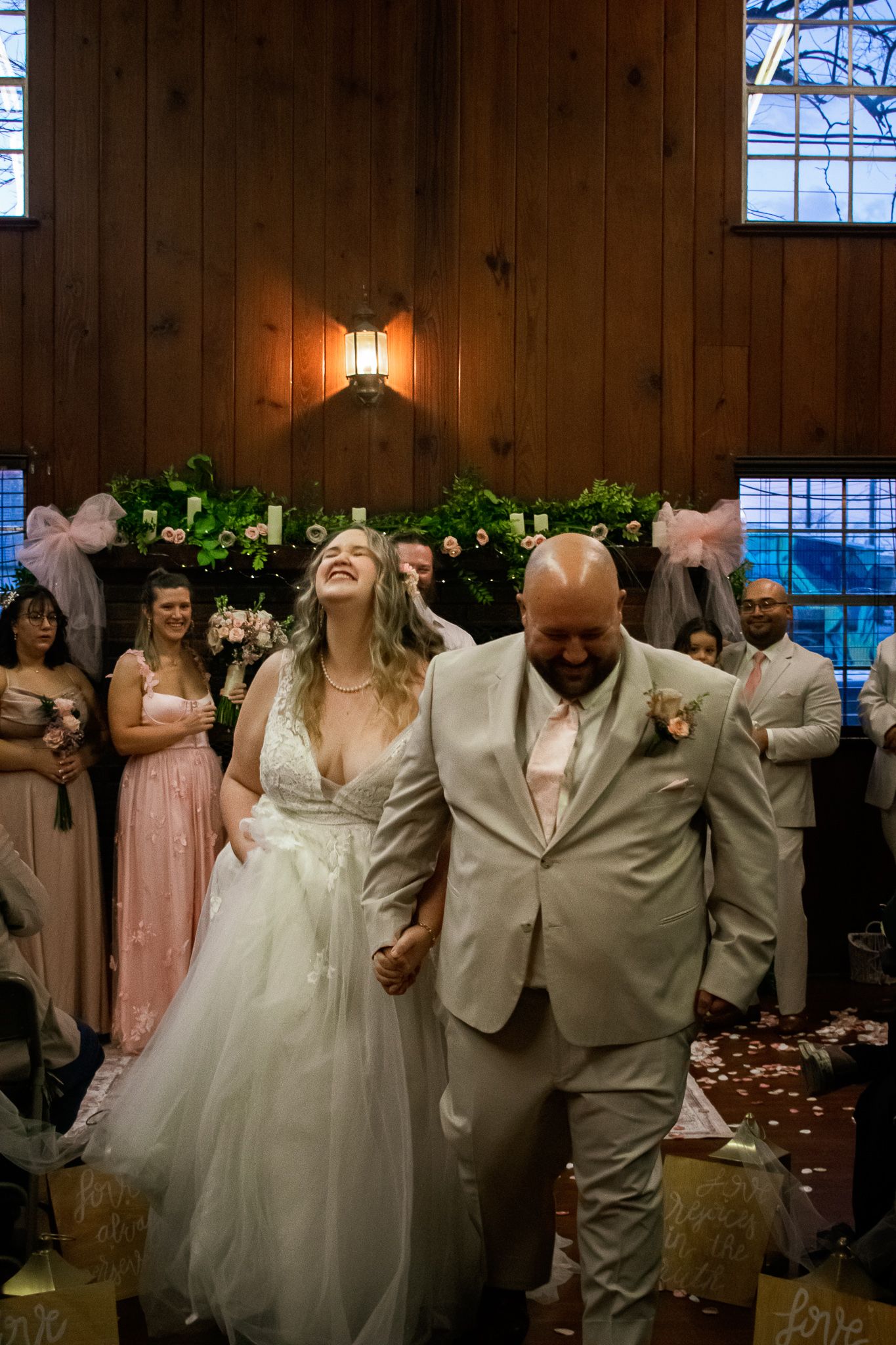 A joyous wedding recessional with the couple walking down the aisle in a wood-paneled venue.