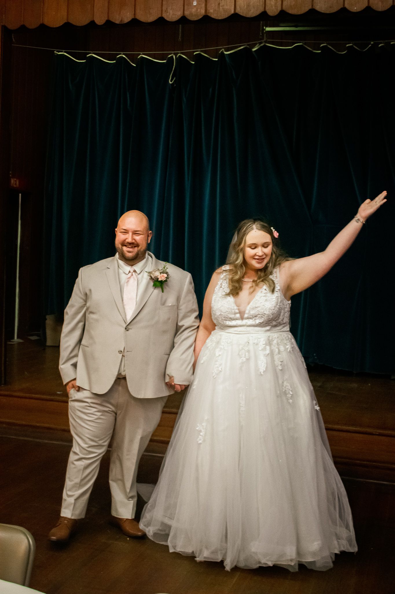 A joyful couple celebrates at their wedding reception, with the bride in a white gown raising her arm in celebration.