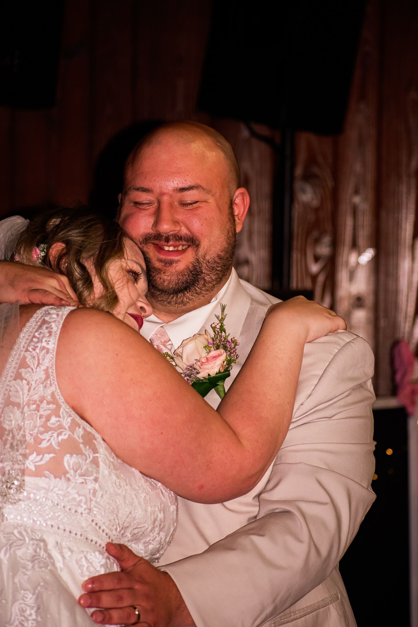 An intimate embrace captured during a wedding celebration with warm lighting and rustic wooden walls.
