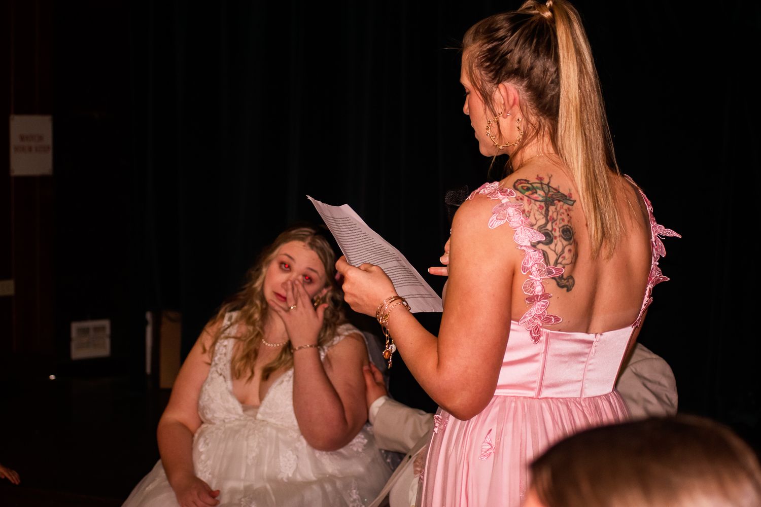 Emotional moment during wedding speech as bridesmaid reads from paper in pink dress.