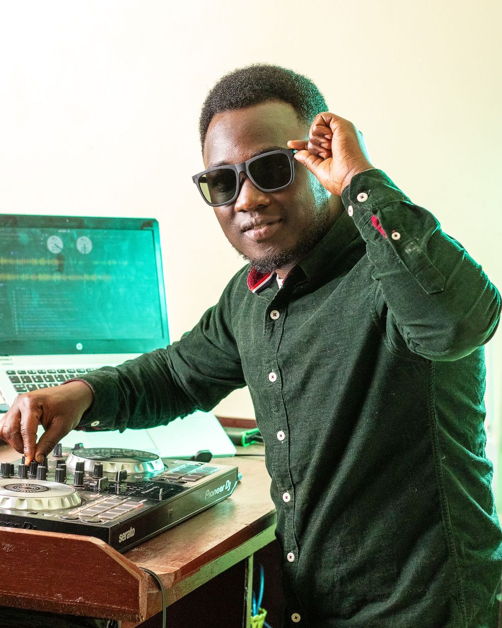 a disk jockey (DJ) poses for photo holding dj kit and his spectacles on another hand facing toward the camera