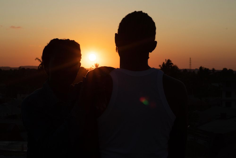 A silhouette photo of 2 people in  orange bright sunset.