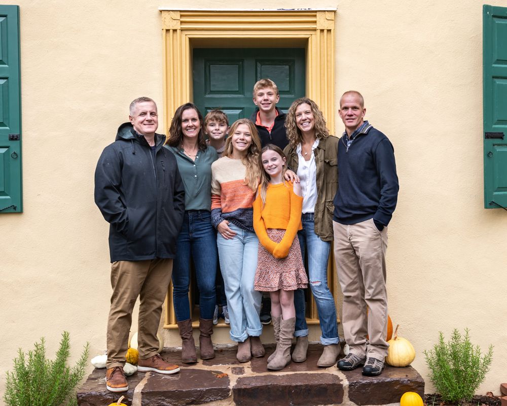 Group gathered on the front steps of a yellow building with green shutters.