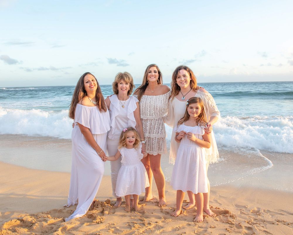 Family group poses together on a sandy beach at sunset wearing coordinated white dresses.