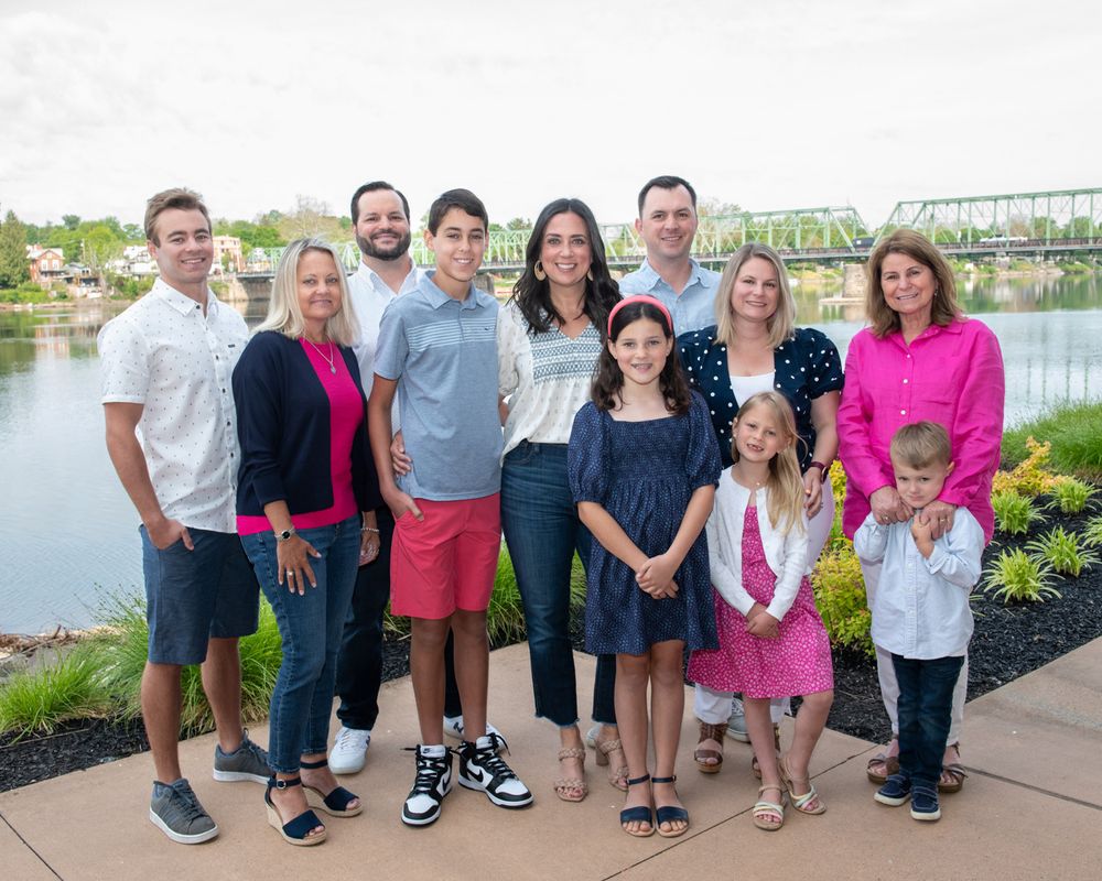 Extended family group poses together outdoors near a river with bridge visible in background.