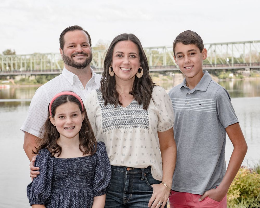 Portrait of a small family group posing together outdoors with a river and bridge behind them.