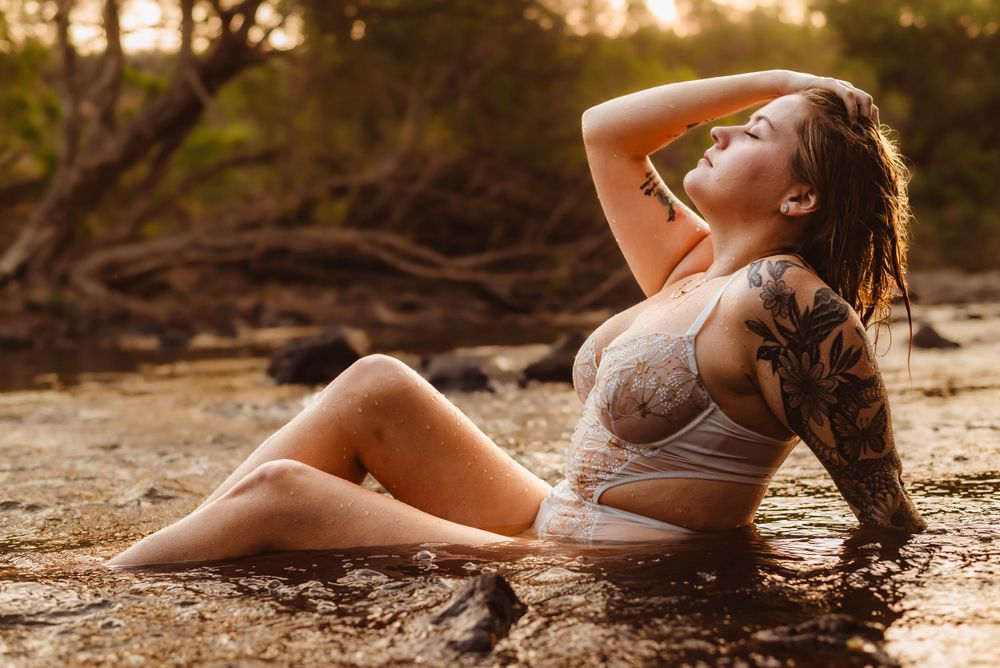 Boudoir photo session in white lingerie at sunset near a river with natural lighting effects.