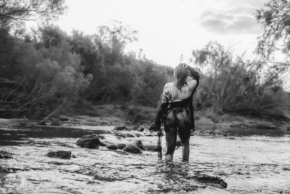 Black and white portrait of couple embracing in shallow river water.